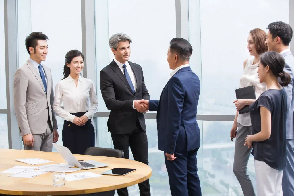 Professionals shaking hands at a business networking event in Singapore while other attendees look on.